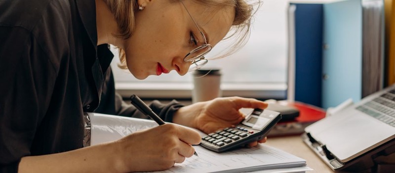 Une personne remplit des documents à son bureau, une calculatrice à la main.