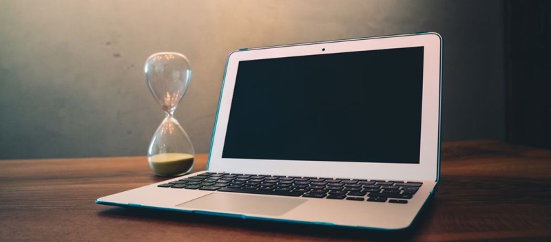 Un ordinateur portable posé sur un bureau, à côté d'un sablier.