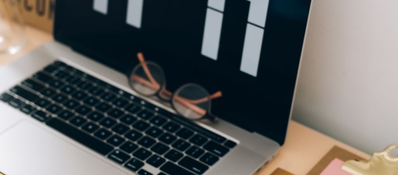 Un ordinateur portable ouvert sur un bureau clair, une paire de lunettes posée à côté.
