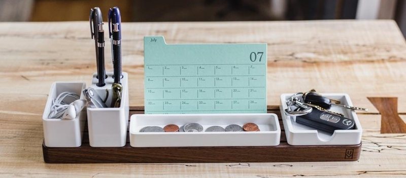 Un organiseur de bureau en bois avec un calendrier mensuel, des stylos, des pièces et des clés.