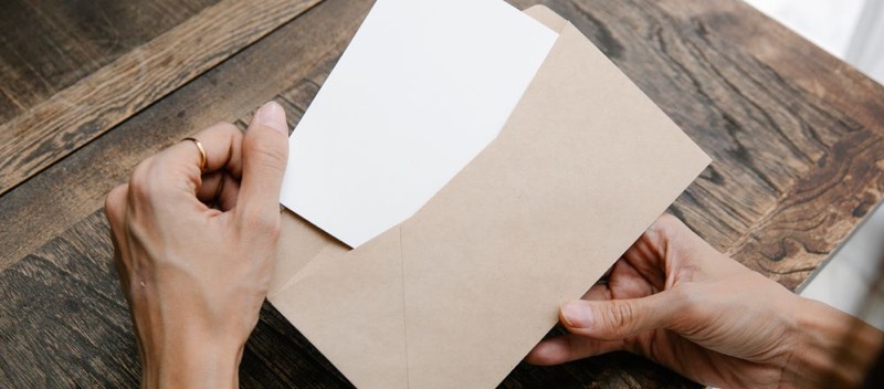 Deux mains ouvrent une enveloppe kraft au-dessus d'un bureau en bois.